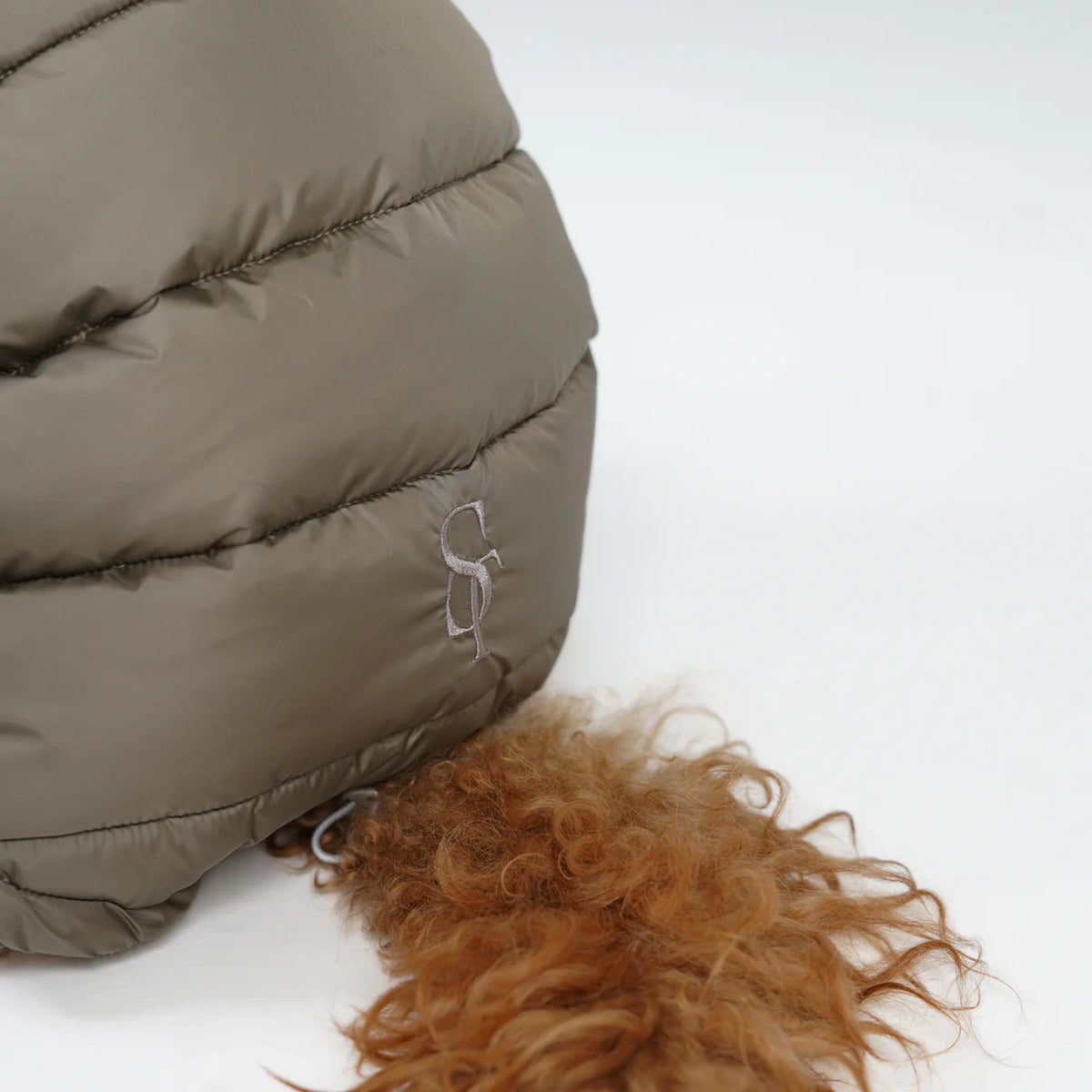 Närbild på det präglade Staey-monogrammet på den taupefärgade, quiltade kappan