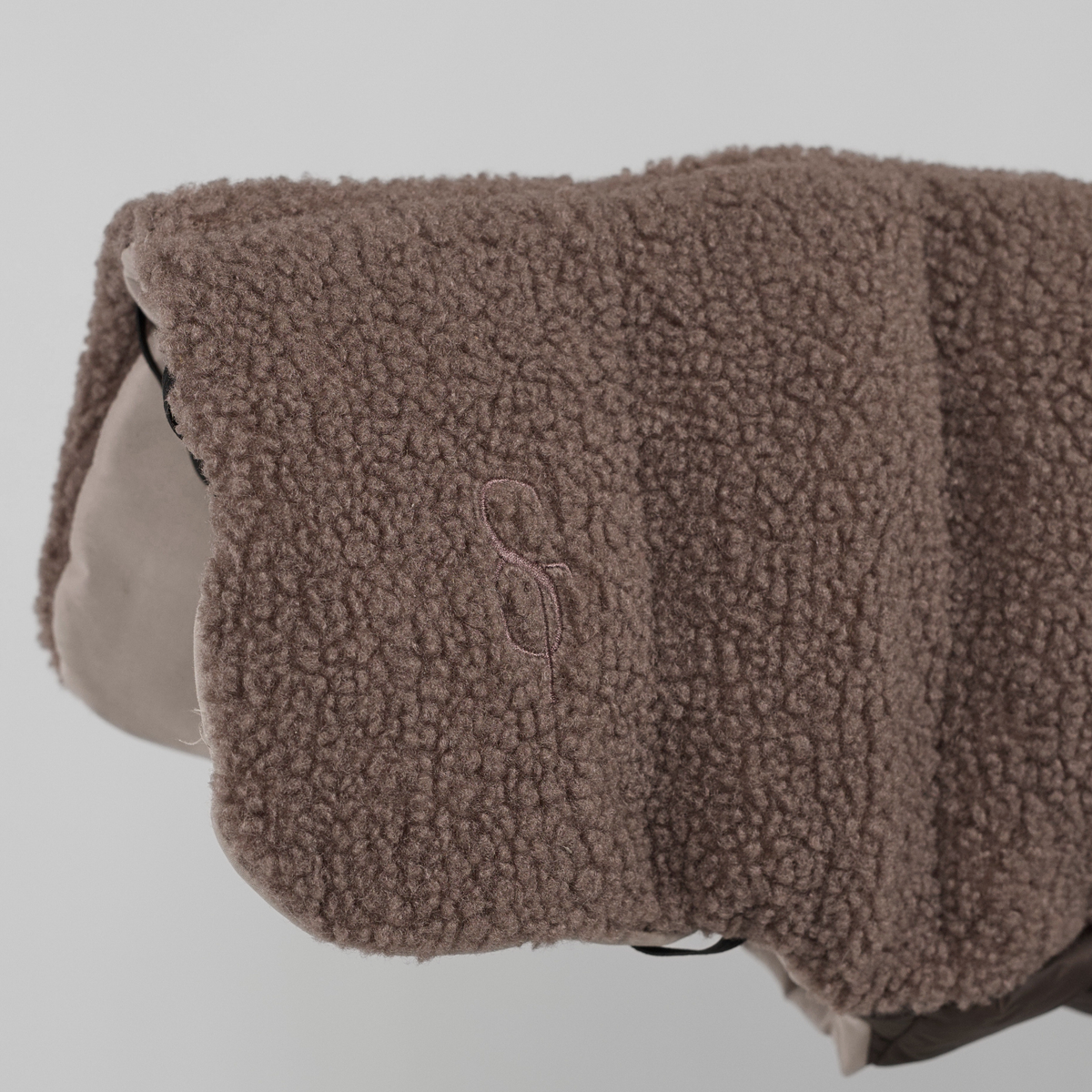 Närbild på det präglade Staey-monogrammet på den taupefärgade teddy-Hundkappa