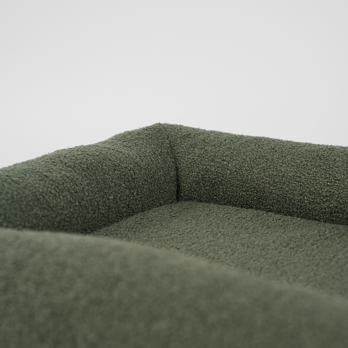 Närbild på ryggstödet och kudden i en moss green bouclé-hundkorg