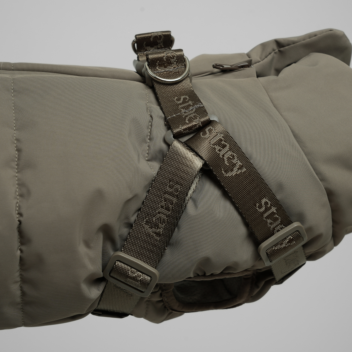 Close-up of the harness webbing on the moss green quilted coat