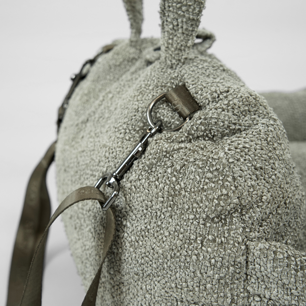 Närbild på säkerhetskopplet och axelremmen på ett bilsäte för hund i Moss Green bouclé